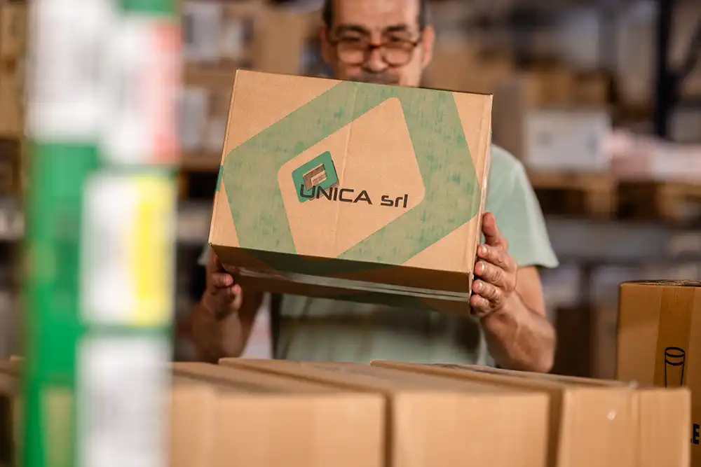 Operatore logistico maneggia un pacco con logo UNICA srl in magazzino, simbolo di affidabilità e consegna efficiente.
