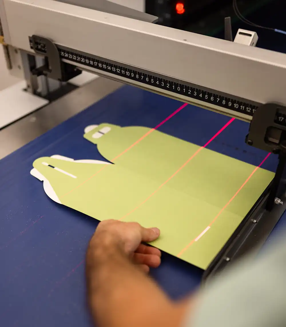 Operatore posiziona fustella sagomata su macchina da taglio con guida laser, simbolo di precisione, personalizzazione e soluzioni di packaging su misura.