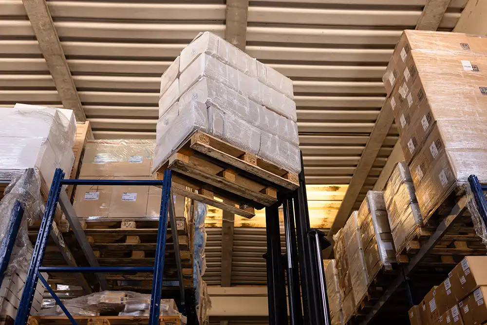 Carrello elevatore solleva pallet imballati all’interno di un magazzino industriale: logistica efficiente, gestione automatizzata e rapidità nelle spedizioni.