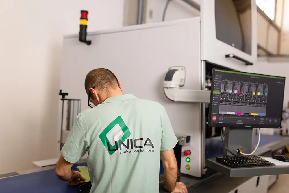 Tecnico UNICA controlla una macchina da stampa digitale con interfaccia a monitor: precisione, tecnologia avanzata e qualità nel packaging personalizzato.